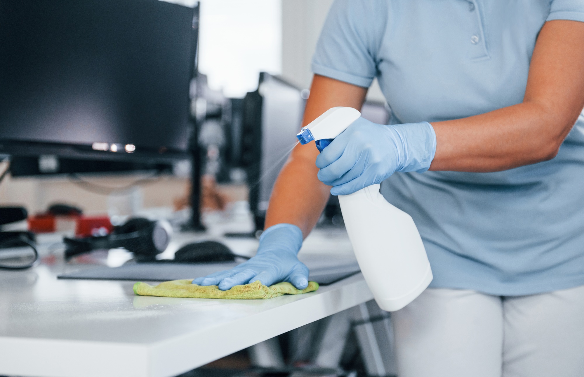Close up view of woman in protective gloves that cleaning tables in the office