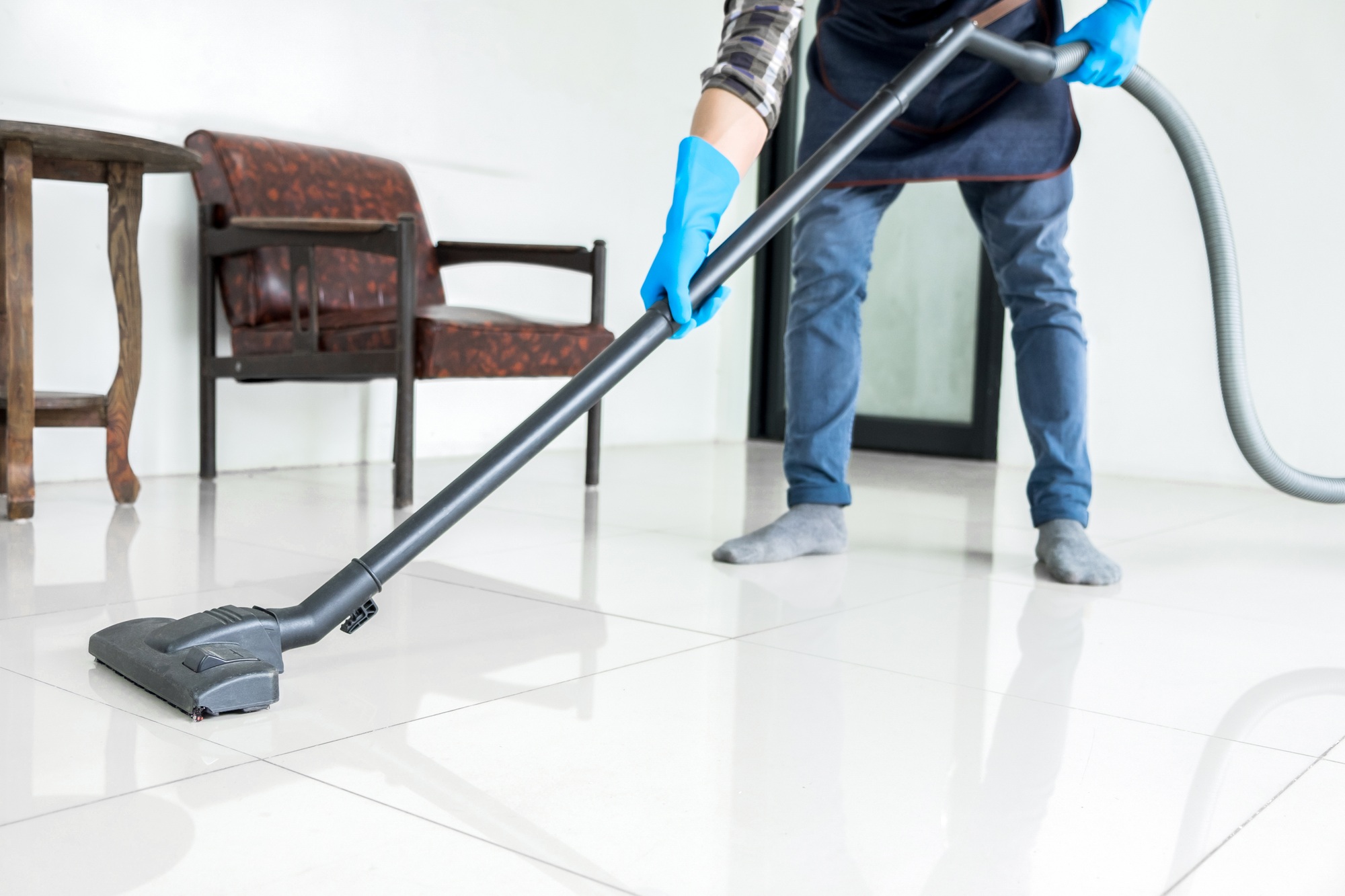 Young attractive man is cleaning vacuum commercial cleaning equipment on floor at home helping wife